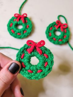 crocheted christmas wreath ornaments being held by a woman's hand with red and green yarn