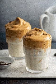 two glasses filled with dessert sitting on top of a white tray next to a cup