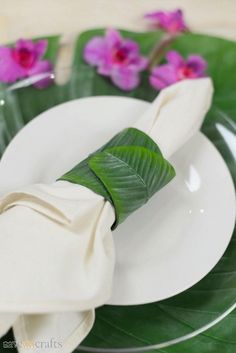 a white plate topped with a green leaf covered napkin next to purple flowers and leaves