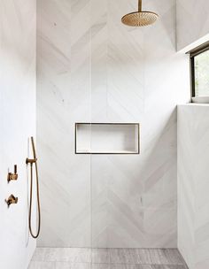 a white bathroom with herringbone tile and gold fixtures on the shower head is featured in this instagram