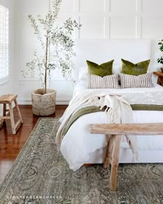 a bed with pillows and blankets on top of it next to a wooden bench in front of a window