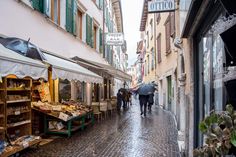 people walking down an alleyway with umbrellas and shops on either side, in the rain