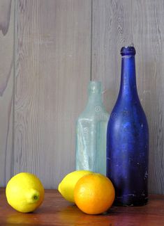 three bottles and two lemons sitting on a table next to each other, with one blue bottle in the background