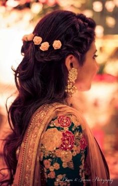 a woman with flowers in her hair wearing a green and gold sari dress, looking off to the side