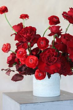 a white vase filled with red flowers on top of a table