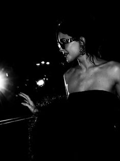 black and white photograph of woman in evening dress looking at cell phone with bright lights behind her