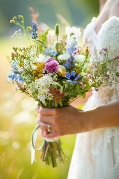 a bride holding a bouquet of wildflowers and daisies in her hands, outdoors