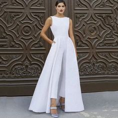 a woman standing in front of a wall wearing a white dress