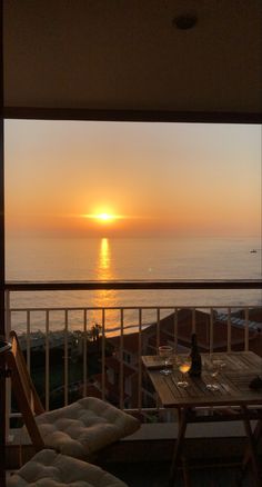 the sun is setting over the ocean from an apartment balcony with table and chairs on it