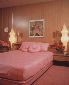 a bed with pink sheets and pillows in a bedroom next to two lamps on either side of the bed