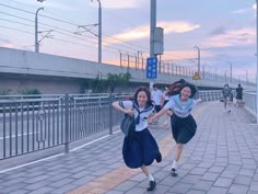 two girls are running down the sidewalk in school uniforms, one is wearing a backpack