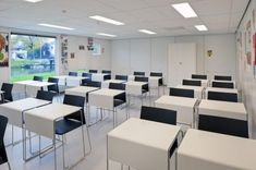 an empty classroom with white desks and black chairs