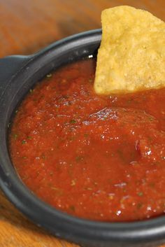 a tortilla chip being dipped with salsa in a bowl on a wooden table