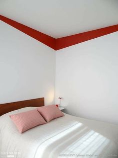 a white bed with pink pillows and red trim on the headboard in a bedroom