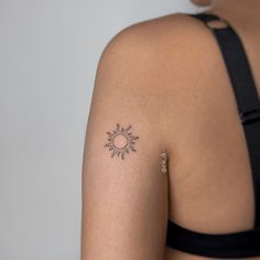 the back of a woman's shoulder with a small sun tattoo on her left arm