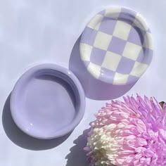 a purple and white checkered plate next to a pink flower on a table top