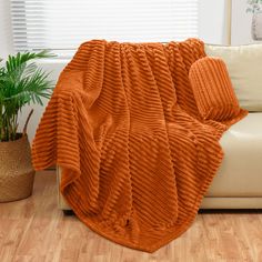 an orange blanket sitting on top of a white couch next to a potted plant