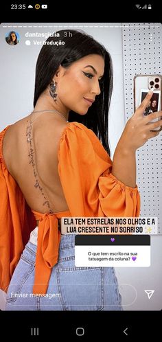 a woman is looking at her cell phone while wearing an orange top and jeans with writing on the back