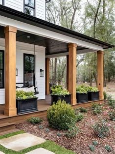 the front porch is covered with plants and potted plants in black planter boxes