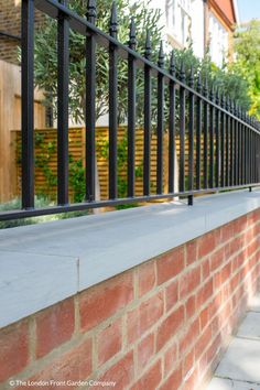 a red brick wall with black iron bars on the top and bottom, in front of a house