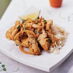 a white plate topped with chicken and rice next to a cup of orange juice on a table