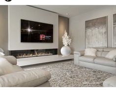 a living room with white furniture and a large flat screen tv mounted on the wall