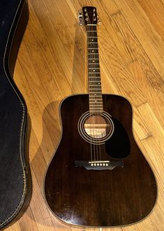 an acoustic guitar is laying on the floor next to a black case and wooden flooring