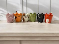 five different colored ceramic cats lined up in a row on a wooden table with white wall behind them