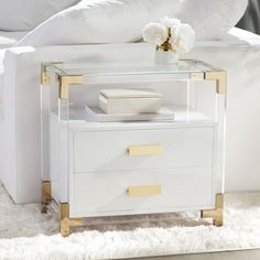 a white and gold nightstand with flowers on it in front of a white bedding