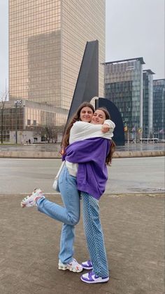 two young women hugging each other in front of tall buildings