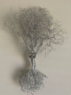 a metal tree sculpture on a wall with its roots growing out of it's base