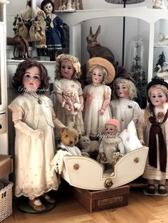 a group of dolls sitting next to each other on top of a wooden floor in front of a white cabinet