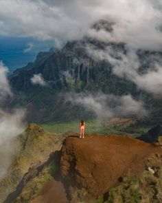 a person standing on top of a mountain with clouds in the sky behind them and mountains below