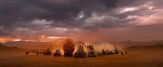 a group of vehicles driving across a desert under a cloudy sky