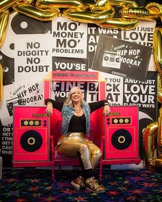 a woman sitting on top of a pink chair in front of a wall with gold balloons