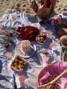 two women sitting on the beach with food and drinks in front of them, including doughnuts