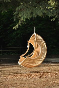 a wooden sculpture hanging from a rope in the middle of a field with trees behind it