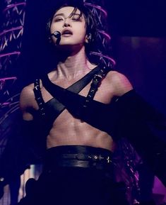 a woman with no shirt on standing in front of a microphone and wearing leather harnesses