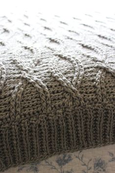 a close up view of a knitted blanket on top of a bed with blue and white flowers