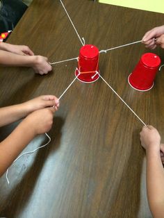 four children are playing with red cups on a wooden table and stringing them together