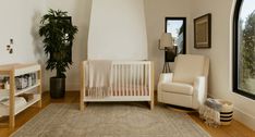 a baby's room with a white crib, chair and potted plant