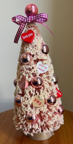 a white christmas tree with red and pink ornaments on it's top, sitting on a wooden table