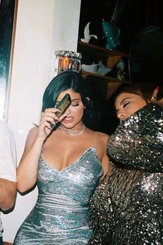 two women and a man standing next to each other in front of a mirror looking at their cell phones