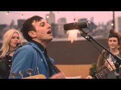 a man singing into a microphone while playing an acoustic guitar in front of other people