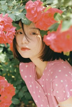 a young woman is posing for a photo in front of some pink flowers and greenery