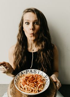 a woman holding a plate of spaghetti in front of her face and making a funny face