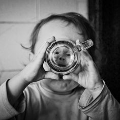 a young child holding a glass cup in front of his face