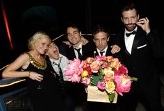 a group of people standing around each other posing for the camera with flowers in front of them