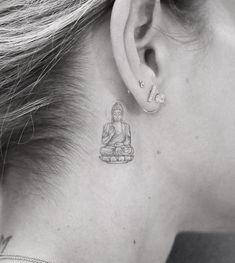 a woman with a small buddha tattoo behind her ear