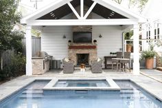 an outdoor living area next to a pool with a tv on the wall and fireplace